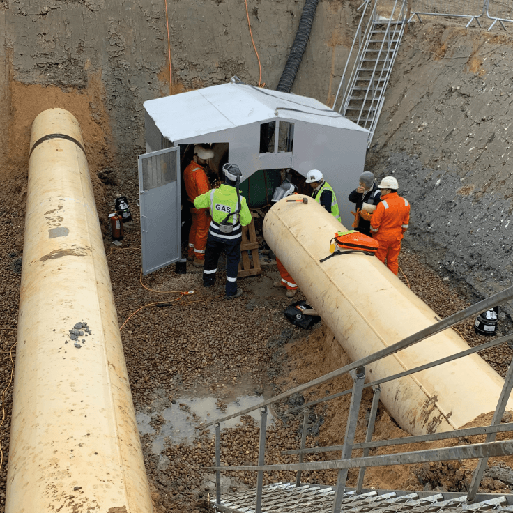 Construction workers stood in large well in ground managing newly laid pipes